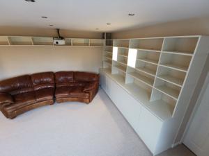 Cinema room formed from ivory paneling with base cupboards, shelves and feature display boxes, lit with led spots