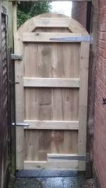 Framed, ledged and braced gate finished in pressure treated gravel boards fitted vertically with an arched top