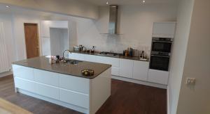 White gloss handleless kitchen with stone worktops on a vinyl floor