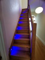Glass and oak staircase with blue string lights on alternate steps that activate when you walk on the stairs